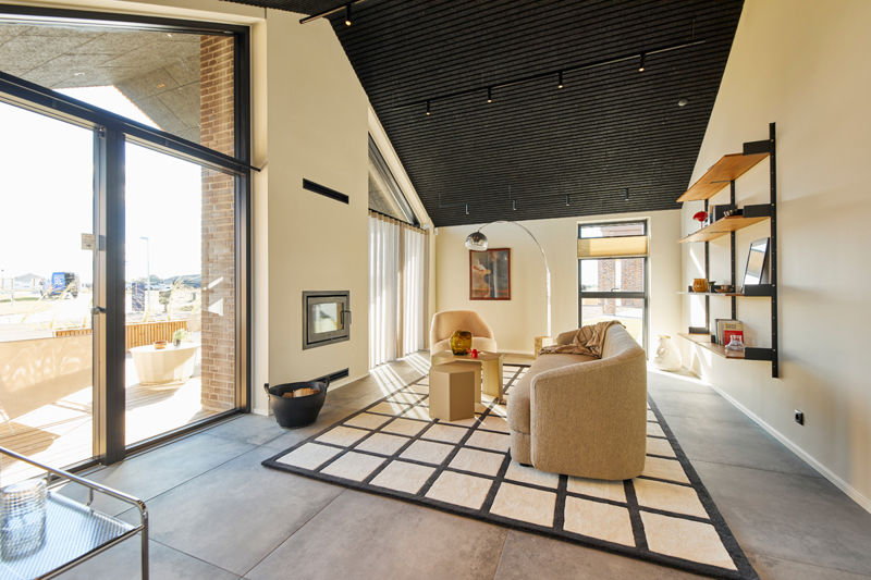 Moderne stue i nybygget barnhouse med pejs, store glaspartier, sort loft, lyse møbler og direkte forbindelse til overdækket terrasse
