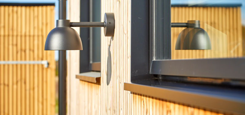 Detalje af sort vindue og udendørslampe på træfacade i nybygget barnhouse med fokus på arkitektur og materialevalg