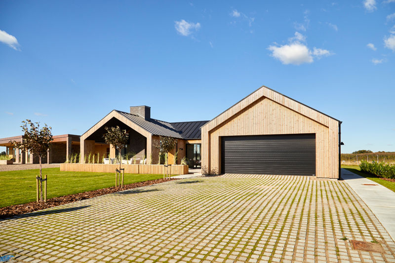 Udvendig garage med stor sort garageport, lodret træbeklædning, sort tag, bred indkørsel med græsarmering og overdækket terrasse ved siden af – inspiration til garage i nybyggeri, carportløsninger og moderne husdrømme fra eurodan-huse.