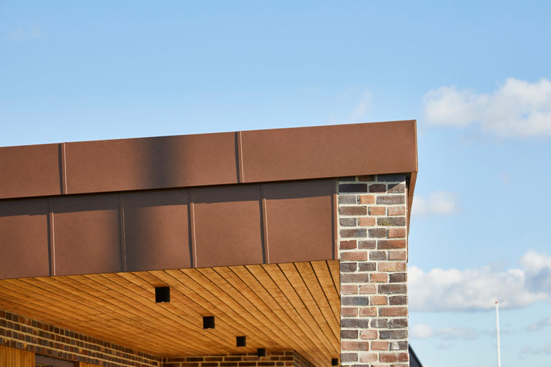 Detalje af udstillingshus fra eurodan-huse med kobberfarvet stern, træloft, murstenssøjle og fladt tag til arkitektonisk nybyggeri og husbyggeri.