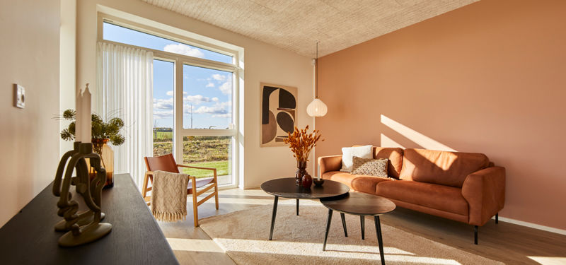 Lys stue i udstillingshus fra eurodan-huse med orange sofa, stor terrassedør, varm vægfarve og træloft til inspiration for nybyggeri og husbyggeri.
