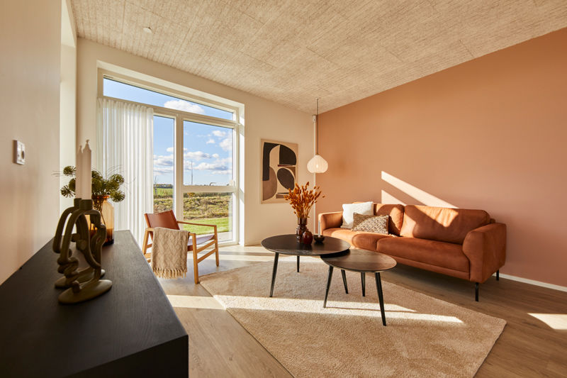Lys stue i udstillingshus fra eurodan-huse med orange sofa, stor terrassedør, varm vægfarve og træloft til inspiration for nybyggeri og husbyggeri.