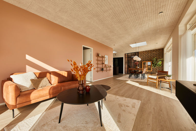 Lyst opholdsrum i udstillingshus fra eurodan-huse med orange sofa, træloft, store vinduespartier og åbent kig til spiseplads til moderne nybyggeri og husbyggeri.