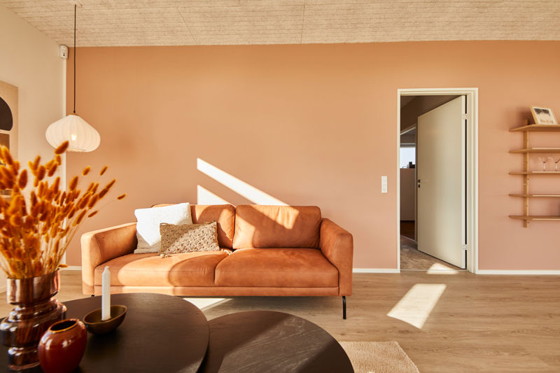 Stue i udstillingshus fra eurodan-huse med orange sofa, varm vægfarve, træloft, rund sofabord og lysindfald til moderne nybyggeri og husbyggeri.