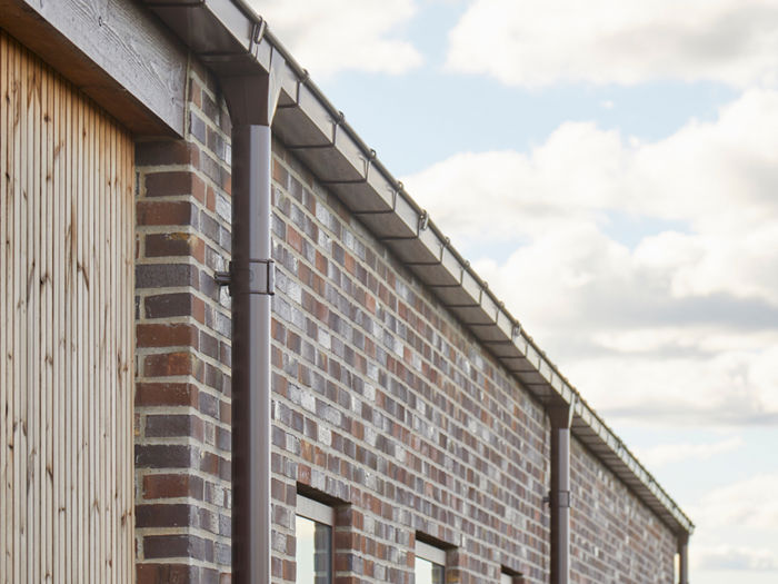 Detalje af facade på udstillingshus fra eurodan-huse med murstensvæg, træbeklædning, tagrende og smalle vinduer til moderne nybyggeri og husbyggeri.