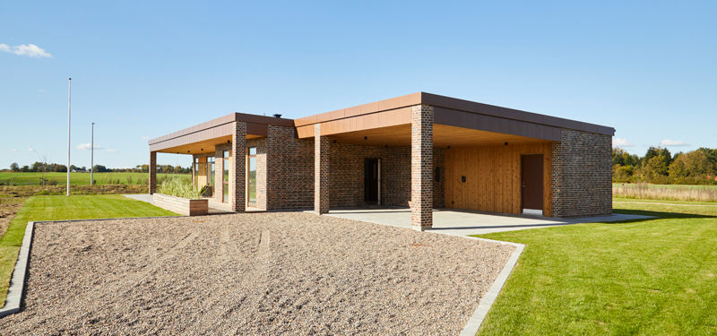 Udstillingshus fra eurodan-huse med fladt tag, murstenssøjler, træbeklædning, carport og grusbelagt indkørsel til moderne nybyggeri og husbyggeri.