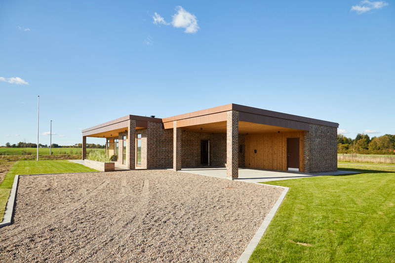 Udstillingshus fra eurodan-huse med fladt tag, murstenssøjler, træbeklædning, carport og grusbelagt indkørsel til moderne nybyggeri og husbyggeri.