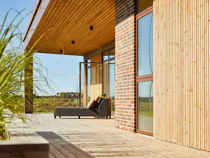 Overdækket træterrasse i udstillingshus fra eurodan-huse med træfacade, murstenssøjle, loungemøbler og store glaspartier til moderne nybyggeri og husbyggeri.