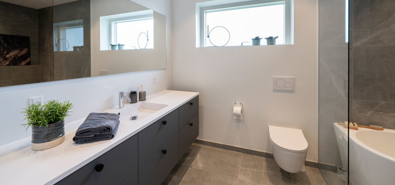 Moderne badeværelse med mørkt vaskemøbel, stort spejl og væghængt toilet i nyt hus.