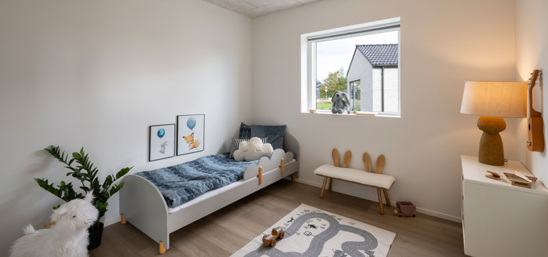 Hyggeligt børneværelse med seng, legetøj og vindue i et familievenligt vinkelhus på 179 m².