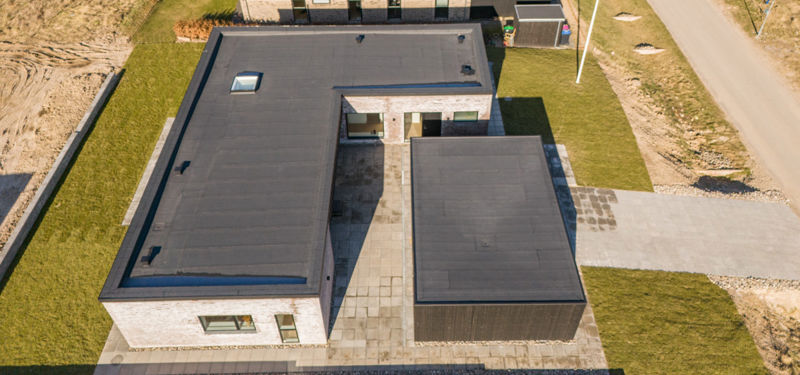 Nybyggeri set fra luften med fladt tag, mørk carport, gårdmiljø og moderne arkitektur