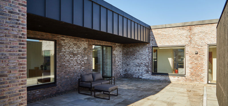 Gårdhave i moderne nybyggeri med murstensfacade, store vinduer og afskærmet terrassemiljø