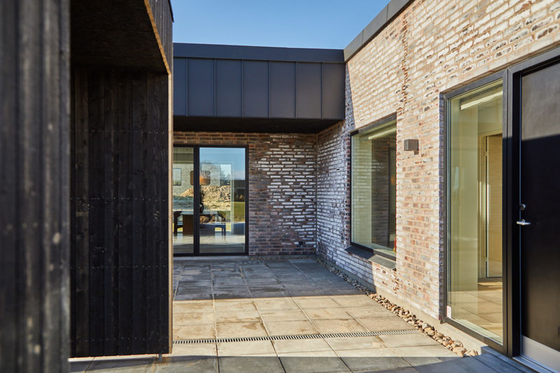 Gårdhave i moderne nybyggeri med murstensfacade, sort træbeklædning og store glaspartier