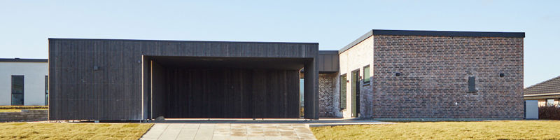 Moderne husbyggeri med mørk carport, fladt tag og minimalistisk facade i mursten og træbeklædning