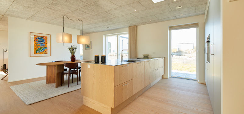 Køkken-alrum i moderne nybyggeri med køkkenø, ovenlys, spiseplads og lyst leverum