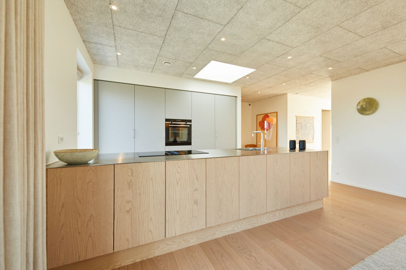 Køkken i moderne nybyggeri med lang køkkenø, træfronter, ovenlys og minimalistisk indretning