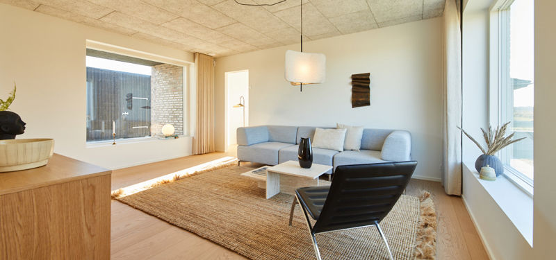 Stue i moderne nybyggeri med store vinduer, sofa, loungestol og naturligt lysindfald