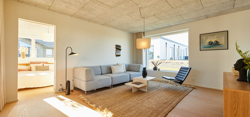Stue i moderne nybyggeri med sofa, loungestol, stort vindue og naturligt lysindfald
