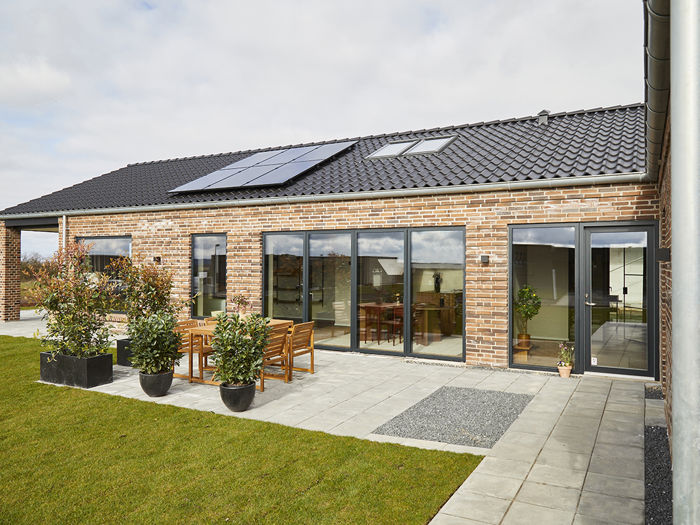 Moderne murstenshus med solceller, ovenlysvindue, store glaspartier og fliseterrasse – inspiration til nybyggeri med eurodan-huse.