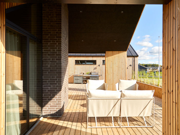 Overdækket træterrasse med loungeområde og udekøkken ved et moderne eurodan-hus.
