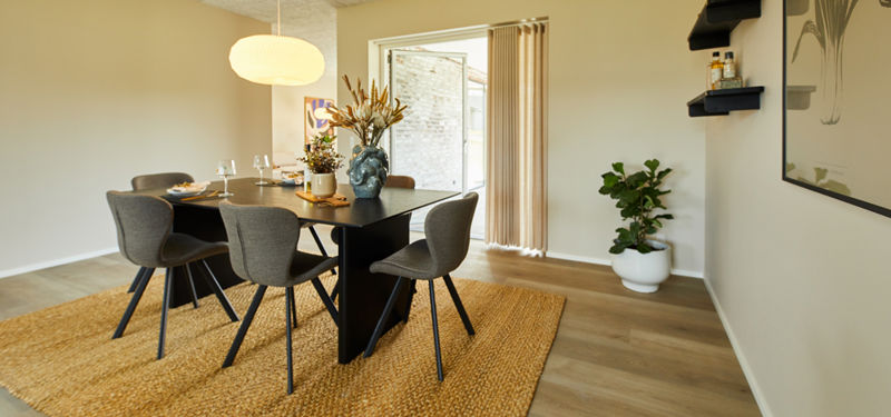 Spiseplads i moderne vinkelhus med sort spisebord, grå stole, stor pendellampe, vævet gulvtæppe og terrassedør – inspiration til personlige husdrømme.