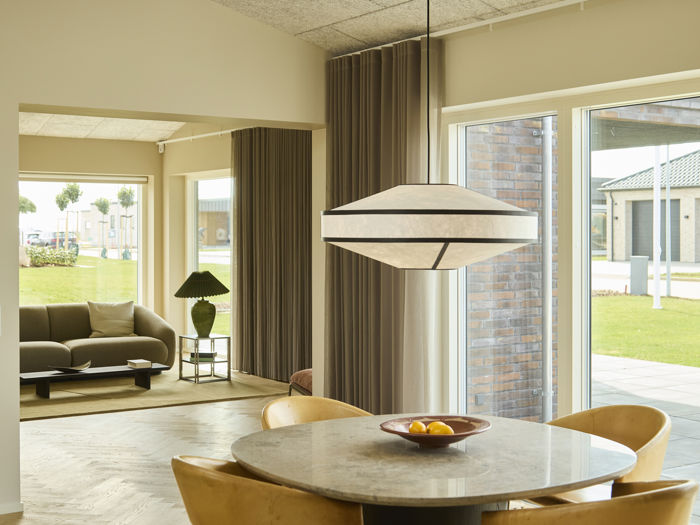 Indbydende spiseplads med rundt spisebord, polstrede stole, stor pendellampe, sildebensgulv og brede vinduespartier med kig til stuen – moderne inspiration til nybyg og husdrømme.