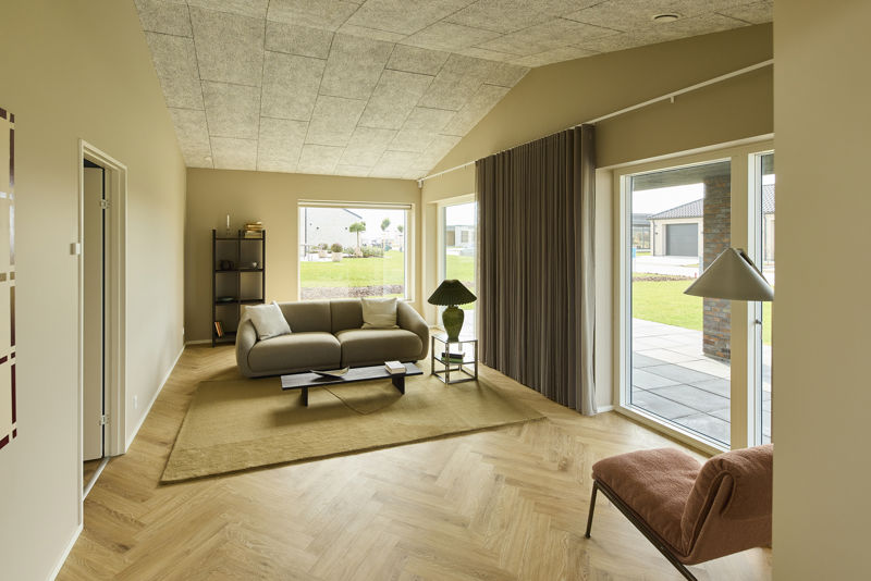 Lys stue med sofa, loungestol, sildebensgulv, lange gardiner og store vinduespartier med udgang til terrassen – indbydende inspiration til moderne nybyg og husdrømme.
