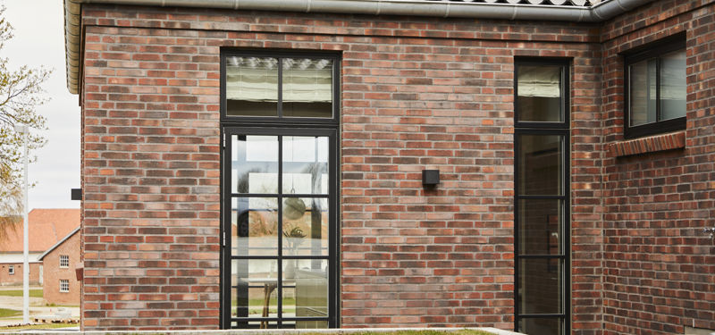 Facadedetalje på moderne nybyg med mørke mursten, høje sorte sprossevinduer og muret gesims – inspiration til et karakterfuldt drømmehus.