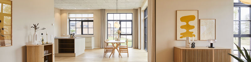 Lyst køkken-alrum og stue i et drømmehus fra eurodan-huse med lyse trægulve, træmøbler, store vinduespartier og varm, moderne indretning.