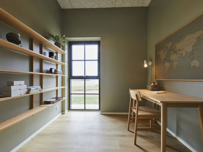 Kontor fra eurodan-huse med lang hyldevæg i træ, grønlige vægge, skrivebord med stol, væglampe, stort verdenskort og højt vindue med sorte sprosser – inspiration til personligt hjemmekontor, nybyggeri og husdrømme med fleksible rum.