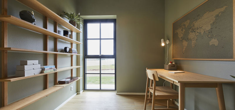 Kontor fra eurodan-huse med lang hyldevæg i træ, grønlige vægge, skrivebord med stol, væglampe, stort verdenskort og højt vindue med sorte sprosser – inspiration til personligt hjemmekontor, nybyggeri og husdrømme med fleksible rum.