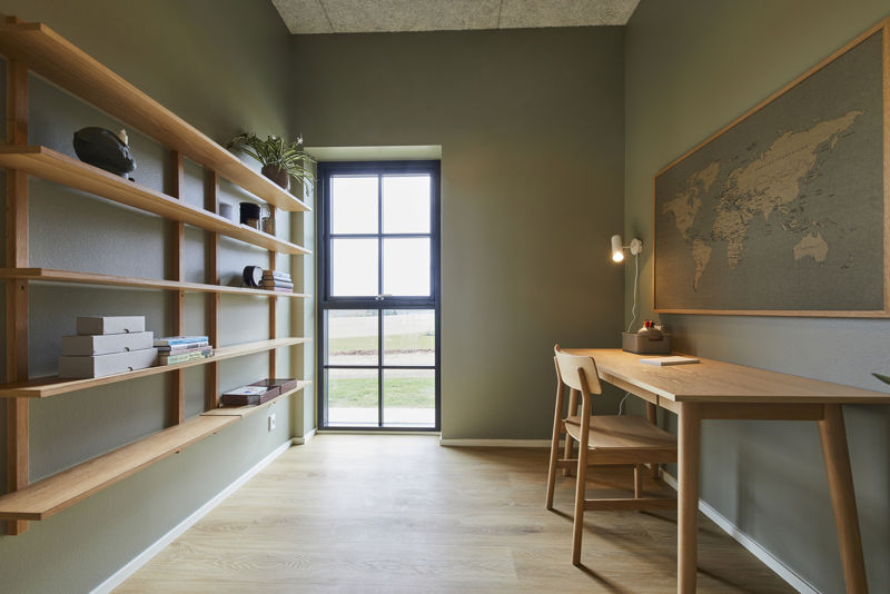 Kontor fra eurodan-huse med lang hyldevæg i træ, grønlige vægge, skrivebord med stol, væglampe, stort verdenskort og højt vindue med sorte sprosser – inspiration til personligt hjemmekontor, nybyggeri og husdrømme med fleksible rum.