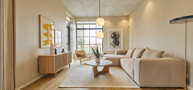 Sofastue fra eurodan-huse med stor beige hjørnesofa, rundt træsofabord, lyst gulvtæppe, træskænk, loungestol ved vinduet og dobbelte runde pendler over sofaområdet – inspiration til nybyggeri, husbyggeri og hyggelige husdrømme.