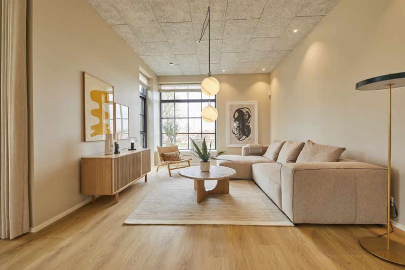 Sofastue fra eurodan-huse med stor beige hjørnesofa, rundt træsofabord, lyst gulvtæppe, træskænk, loungestol ved vinduet og dobbelte runde pendler over sofaområdet – inspiration til nybyggeri, husbyggeri og hyggelige husdrømme.