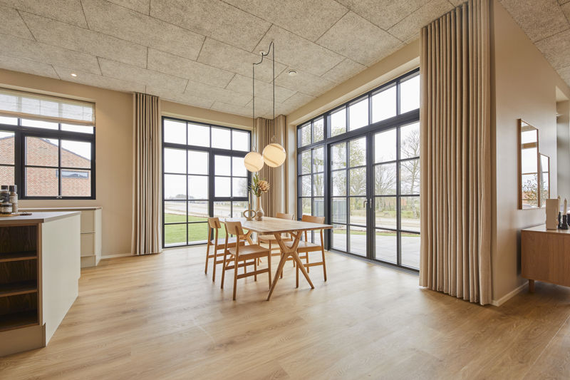 Køkken-alrum fra eurodan-huse med spiseplads ved store sorte vinduespartier, lyse gardiner fra loft til gulv, træbord, træstole, runde pendellamper og udsyn til terrasse – konkret inspiration til nybyggeri og husdrømme med naturligt lys.