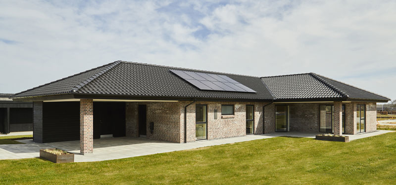 Moderne vinkelhus i mursten med mørkt valmtag, solceller, integreret carport og flisebelagt terrasse – inspiration til nybyg og familiens husdrømme.