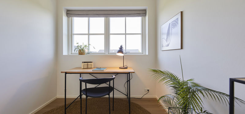 Lille kontor i nybygget hus fra eurodan-huse med skrivebord, stol, plante, rundt tæppe og sprossevindue som fleksibelt rum til husdrømme