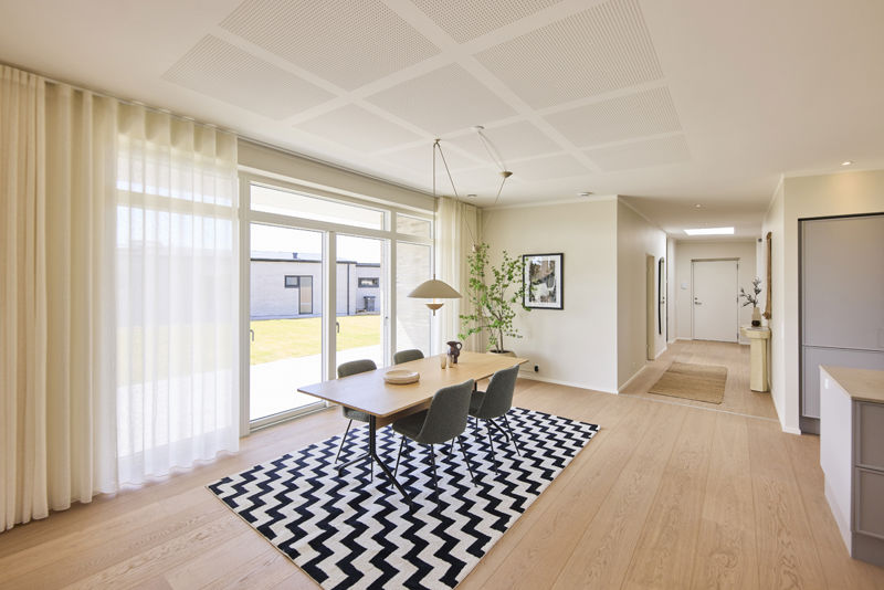 Visualisering af spiseplads i køkken-alrum fra eurodan-huse med langt spisebord, polstrede stole, pendellampe over bordet, store vinduespartier, lyst gulv og åben forbindelse videre mod køkken og opholdsrum – inspiration til nybyggeri, husbyggeri og husdrømme med samlet alrum.