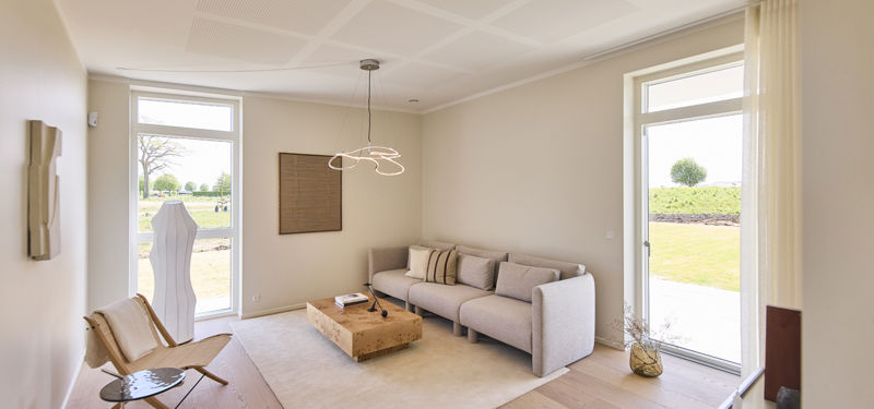 Stue fra eurodan-huse med lys sofa, lavt træsofabord, beige gulvtæppe, loungestol, store gulv-til-loft vinduer, havedør og skulpturel loftlampe – inspiration til nybyggeri, husbyggeri og lyse opholdsrum i et nybygget hus.