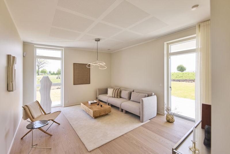 Stue fra eurodan-huse med lys sofa, lavt træsofabord, beige gulvtæppe, loungestol, store gulv-til-loft vinduer, havedør og skulpturel loftlampe – inspiration til nybyggeri, husbyggeri og lyse opholdsrum i et nybygget hus.