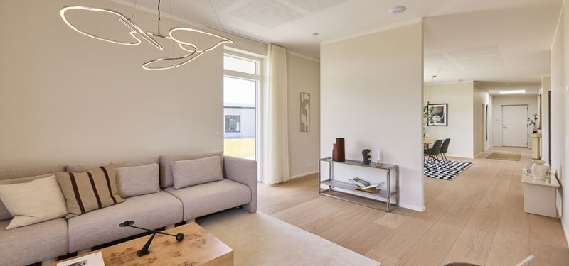 Stue i nybyggeri med trægulv, moderne sofa, dekorativ pendel og skillevæg mellem stuen og køkken-alrummet.