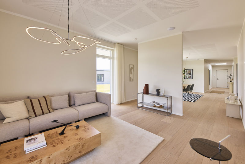 Stue i nybyggeri med trægulv, moderne sofa, dekorativ pendel og skillevæg mellem stuen og køkken-alrummet.