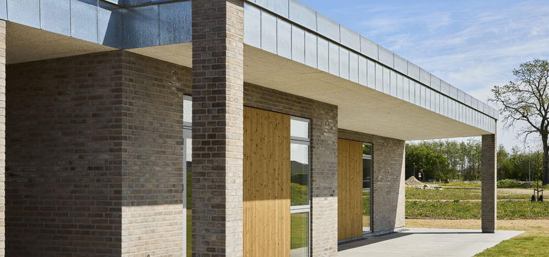 Moderne længehus i nybyggeri med murstensfacade, trædetaljer og overdækket terrasse – inspiration til stilrene husdrømme.
