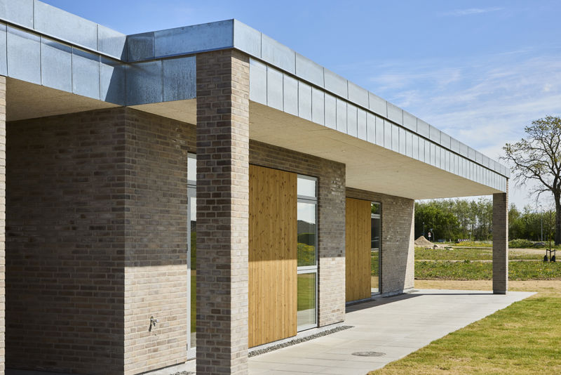 Moderne længehus i nybyggeri med murstensfacade, trædetaljer og overdækket terrasse – inspiration til stilrene husdrømme.