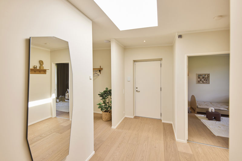 Indgangsparti fra eurodan-huse med stort ovenlys, lys trælook gulv, fuldhøjt spejl, plante i flettet kurv og åbning til børneværelse – inspiration til en lys entré i nybyggeri og gennemtænkte husdrømme.