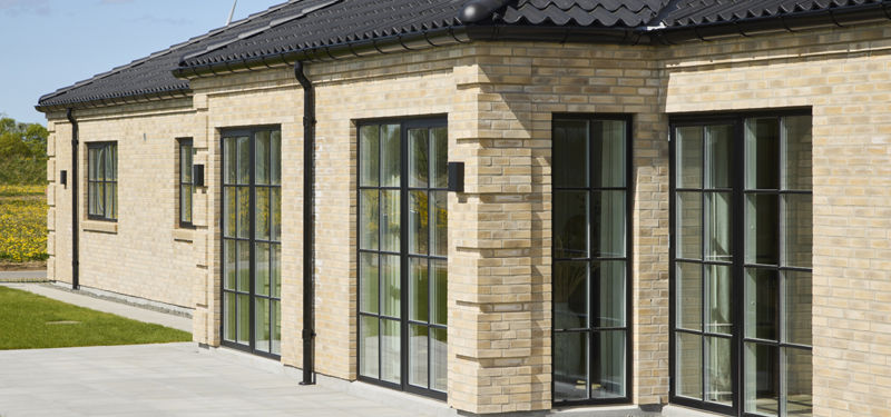 Murstenshus fra eurodan-huse med sort tegltag, store sprossede vinduespartier og flisebelagt terrasse, der giver inspiration til klassisk nybyggeri med moderne detaljer.