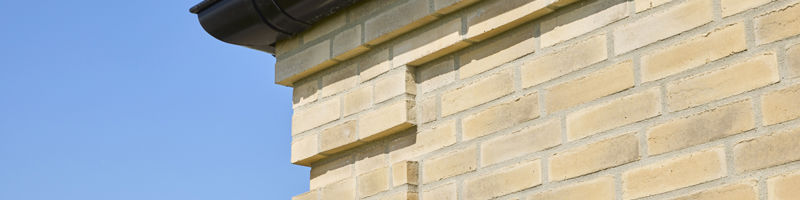 Detaljebillede af murstensfacade på udstillingshus fra eurodan-huse med lyse mursten, sort tagrende og blå himmel, der viser materialevalg til moderne nybyggeri.
