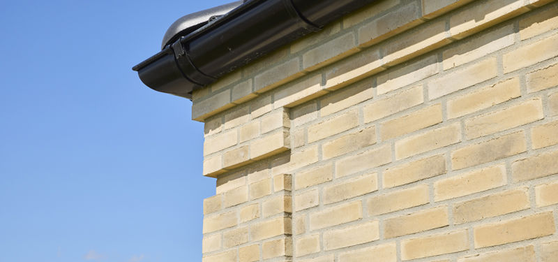 Detaljebillede af murstensfacade på udstillingshus fra eurodan-huse med lyse mursten, sort tagrende og blå himmel, der viser materialevalg til moderne nybyggeri.