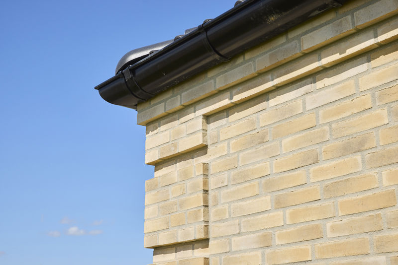 Detaljebillede af murstensfacade på udstillingshus fra eurodan-huse med lyse mursten, sort tagrende og blå himmel, der viser materialevalg til moderne nybyggeri.