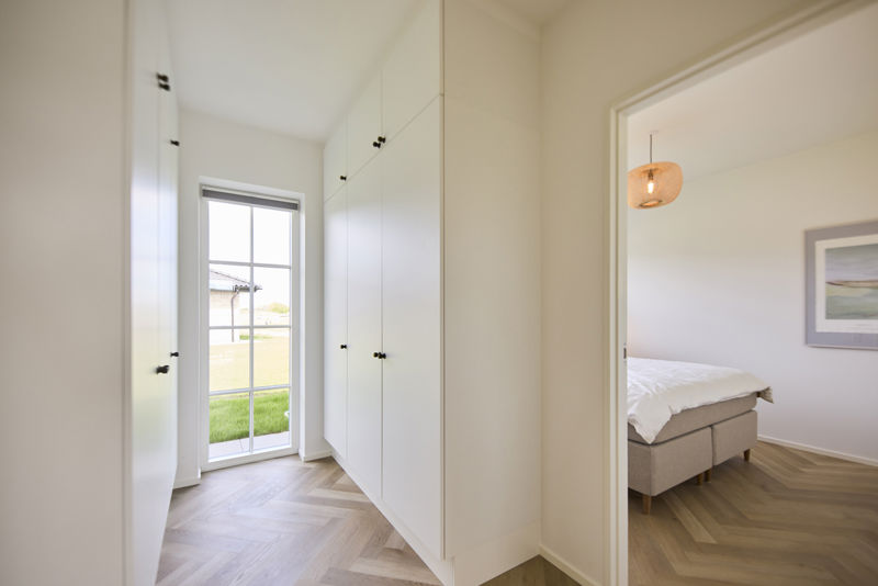 Walk-in og soveværelse i udstillingshus fra eurodan-huse med indbyggede skabe, glasdør og sildebensgulv, der giver inspiration til opbevaring, nybyggeri, husbyggeri og en gennemtænkt planløsning i et nyt familiehus.